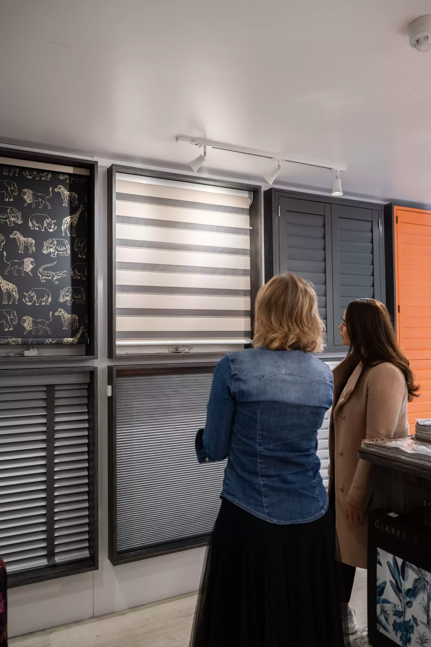 Two people standing before various styles of shutters and blinds.