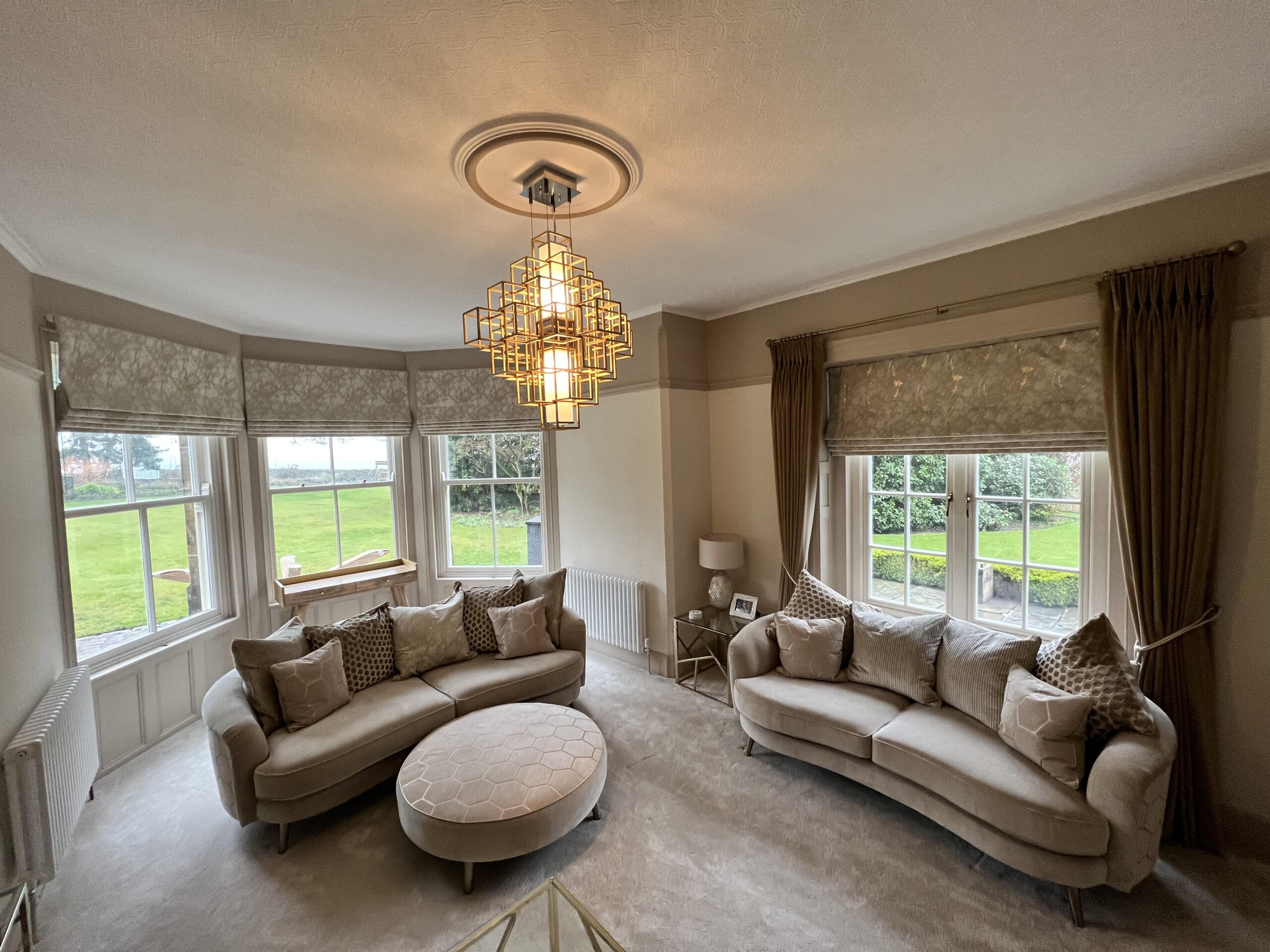 An elegant living room with grey patterned blinds hanging over the windows. On one of the windows a pair of grey curtains accompanies the blinds.