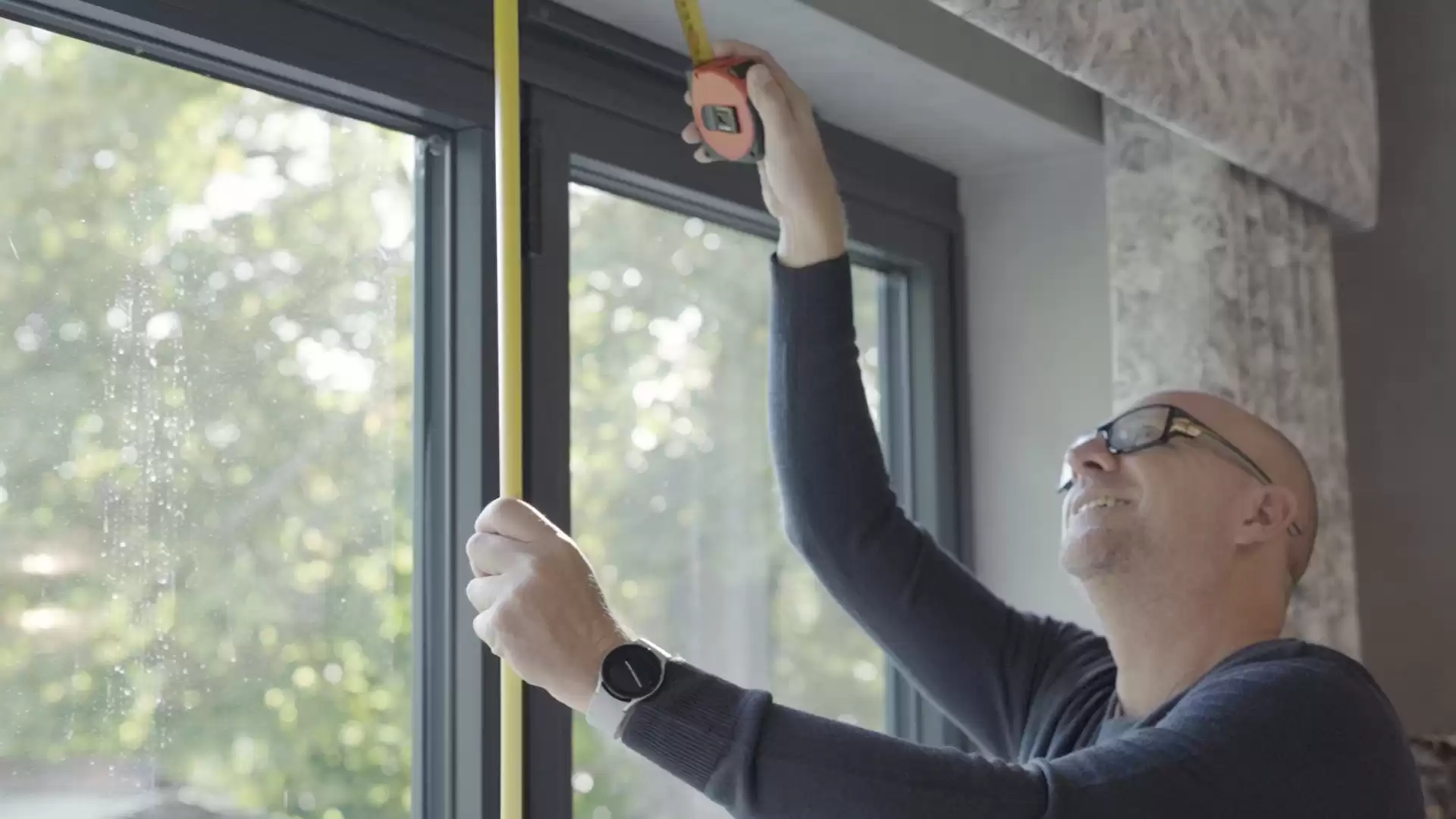 A man measuring a window with a tape measure.