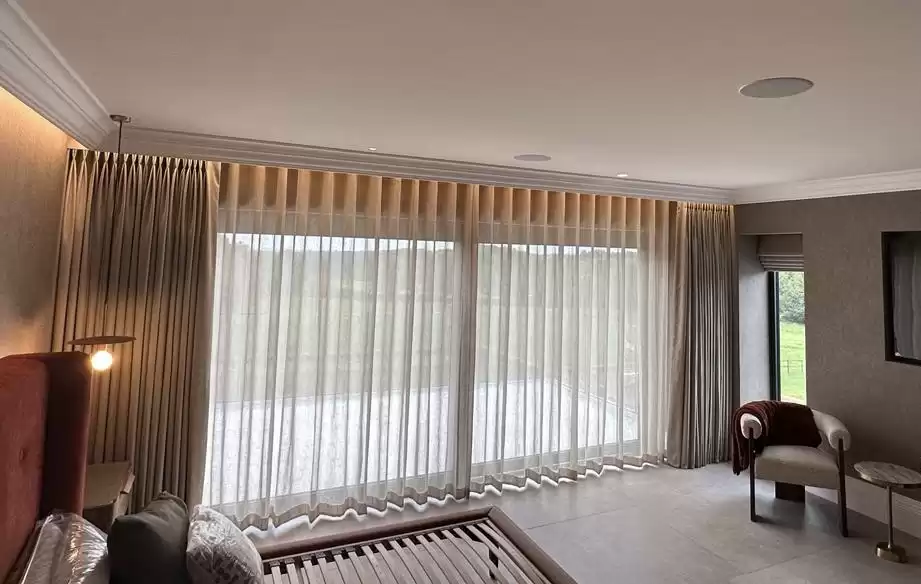 A large window, covered by floor to ceiling sheer beige curtains.